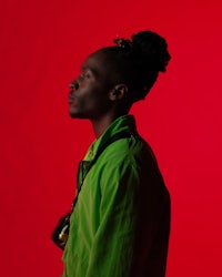 a man with dreadlocks standing in front of a red background